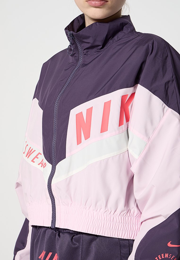 Rompevientos Nike con un cuello alto, hecho de una tela ligera. En colores bloqueados de morado oscuro, rosa claro y blanco; presenta acentos de logotipo llamativos.