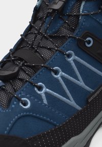 Κοντινή λήψη μπλε αδιάβροχου πεζοπορικού παπουτσιού με μαύρα και γκρι κορδόνια και ενισχυμένες τρύπες κορδονιών σε υφή σόλας.