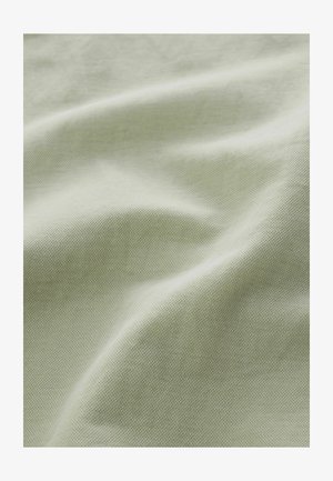 Šviesiai žalia tekstūruota medžiaga su matoma smulkia pynimo struktūra ir minkštais klostėmis, kurios sukuria švelnias šešėlius.