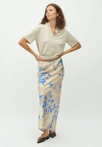 Beige gebreide poloshirt met korte mouwen, gecombineerd met een lange bloemenrok met blauwe patronen op een beige achtergrond. Bruine puntige ballerina's.