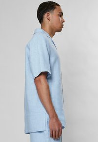 Camicia azzurra a maniche corte con colletto, realizzata in un tessuto a trama, dotata di spacchi laterali e di una vestibilità rilassata.