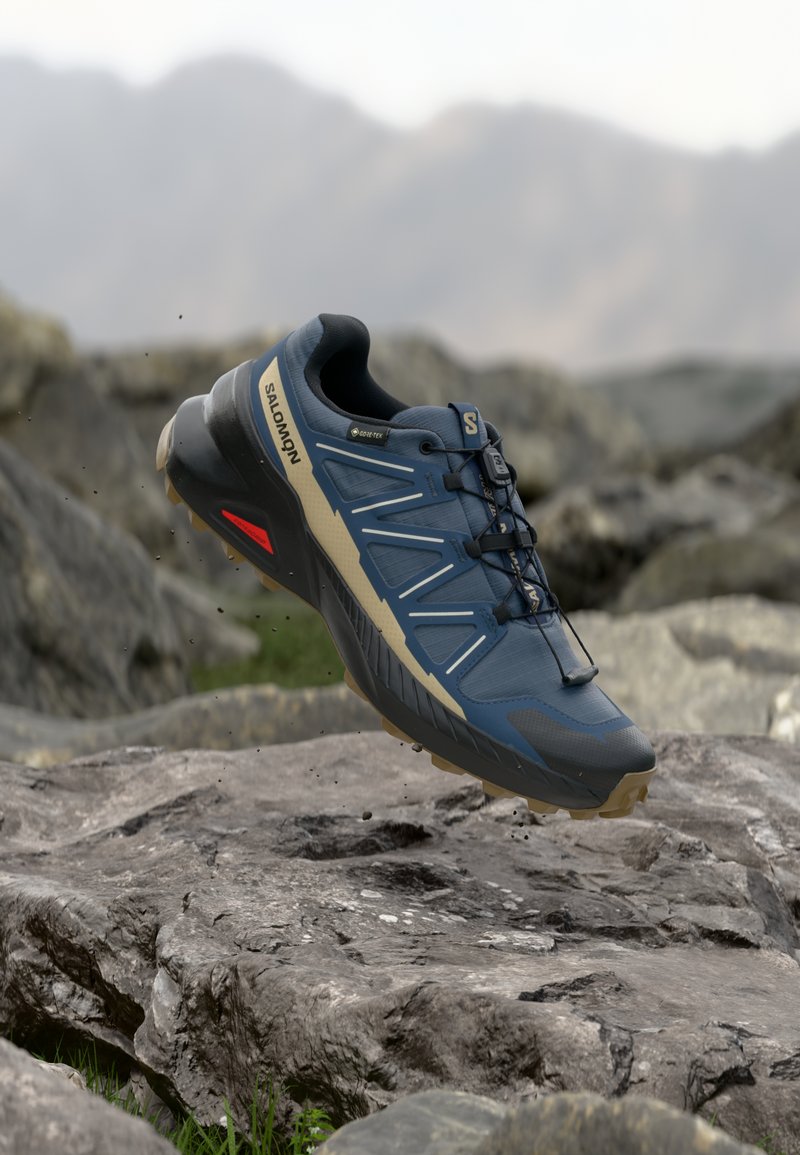 Modrá a béžová turistická obuv Salomon s Gore-Texem, vzhůru nad skalnatým terénem, s rozmazaným horským pozadím.