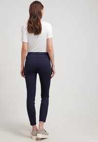 Marina blå byxor med en slät yta, sidofickor och en smal bendesign. Bärs med en vit t-shirt och ljusa skor.