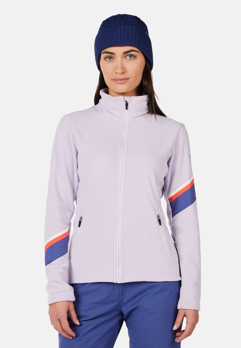 Giacca in pile viola chiaro con colletto alto, chiusura con zip e due tasche laterali. Presenta righe rosse e blu sulle maniche.