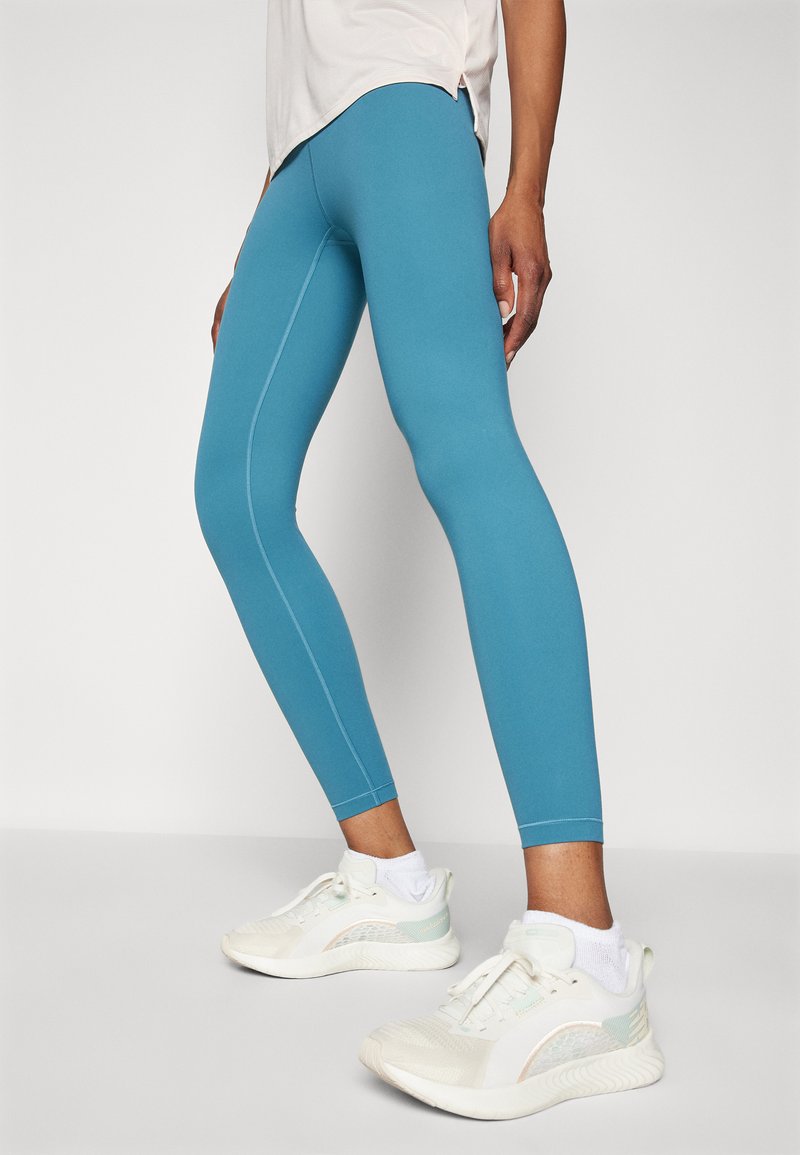 Leggings turquoise avec des coutures plates, modelés pour épouser le corps. Associés à des baskets blanches avec des accents bleu clair et des semelles texturées.