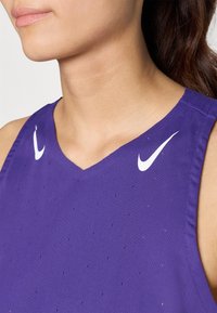 Débardeur de sport violet avec un col en V, tissu perforé pour la respirabilité et accents du logo Nike blanc sur les épaules.