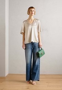 Beige satinv-hals topp, vide ben blå denim jeans og en liten grønn håndveske med klaffhåndtak. Glatt tekstur, uformell design.