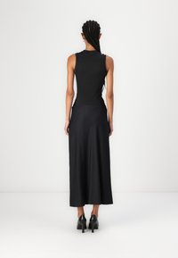 Robe noire sans manches avec un haut ajusté et une jupe fluide jusqu'aux chevilles. Texture lisse, design minimaliste et sans motifs visibles.