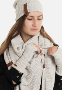 Beige gebreide beanie met geribbelde textuur, bijpassende sjaal in chunky knit en vingerloze handschoenen. Bevat lederen labelaccenten en knoopdetails.