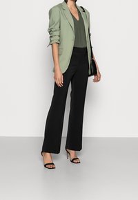 Ljusgrön skräddarsydd blazer över en mörkgrön topp, kombinerad med svarta vida byxor och svarta remsandaler. En enkel svart handväska.