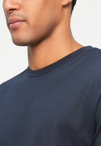 T-shirt girocollo blu navy realizzato in tessuto morbido, con una texture liscia e maniche corte, dal design semplice e classico.