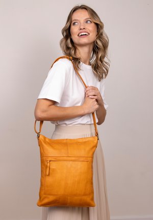 Dzeltena ādas crossbody soma ar strukturētu virsmu, aprīkota ar priekšējo rāvējslēdzēja kabatu un garu regulējamu siksnu. Izveidota ar elegantu, minimālistisku formu.