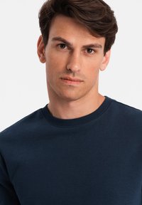 Navy blå sweatshirt lavet af blødt stof, med en ribbet halsudskæring. Designet er enkelt uden mønstre eller accenter.