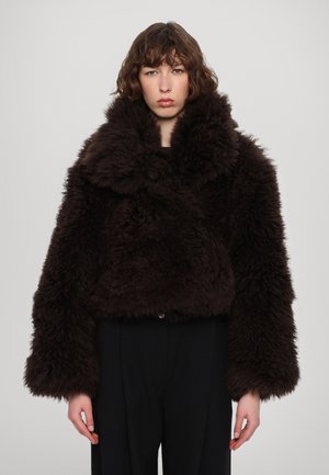 Braune, zottelige Kunstfelljacke mit weitem Kragen, verkürztem Design und oversized Ärmeln, kombiniert mit schwarzen Hosen.