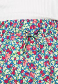 Shorts fleuris en bleu avec un motif vibrant de fleurs rouges, roses et blanches. Dotés d'une taille élastique avec un lien décoratif.