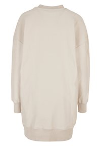 Pull ample beige clair avec texture côtelée, présentant un col montant et des manches longues avec poignets côtelés. Design simple et minimaliste.