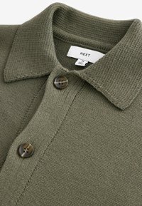 Polo tricotat de culoare verde măsliniu cu un finisaj texturat, având un guler clasic și două nasturi maro, etichetat cu tag-ul "NEXT".