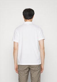 Hvid polo shirt med klassisk krave, korte ærmer og lige kant. Stoffet ser glat ud uden synlige mønstre eller detaljer.