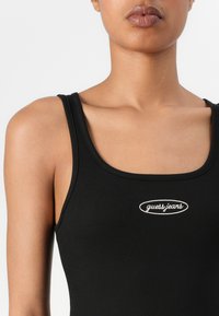Čierny rebrovaný tielko s okrúhlym výstrihom a úzkymi ramienkami, so bielou vyšitou logom "guess jeans" na prednej strane.