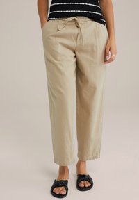 Beige, lightweight, cotton blend trousers with an elastic waistband and drawstring. Straight-leg design, cuffed ankles, and side pockets.