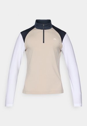 Top bege de mangas compridas com colarinho de meio fecho. Mangas raglan azul-escuras que passam para punhos brancos. Tem um pequeno logo no peito.