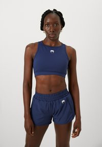Conjunto de top corto atlético y pantalones cortos en color azul marino, hecho de una tela elástica con un logo en el pecho y la cintura. Textura suave, diseño ajustado.