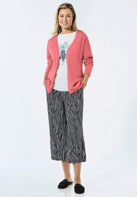 Korallefarbener Cardigan über einem weißen Grafik-T-Shirt, kombiniert mit weit geschnittenen Hosen mit schwarz-weißen Mustern und schwarzen Slippern.