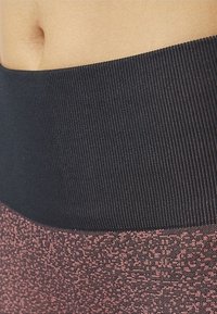 Leggings deportivos de cintura alta con una cinturilla de canalé negra gruesa y una sección inferior texturizada en rosa con un patrón moteado.