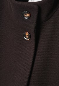 Manteau en laine brun foncé avec deux grands boutons brun et noir attachés près du col.