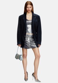 Blazer in denim, top canotta metallico argento, gonna mini lucente argentata e tacchi metallici. Accentuato da una piccola borsa argentata.
