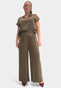 Maglietta oversize verde oliva con maniche corte e scollo a V, abbinata a pantaloni a gamba larga. Tessuto morbido, pieghe sottili, completata da scarpe rosse a punta.