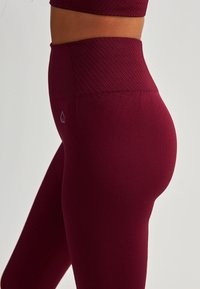 Bordowe legginsy sportowe z ribbowanym, wysokim pasem i gładką fakturą materiału, zaprojektowane z myślą o elastyczności i komforcie podczas treningów.