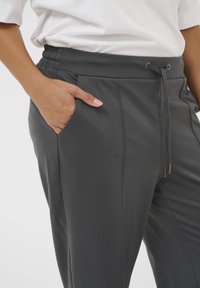 Grijze sweatpants met een elastische tailleband, trekkoorddetail en zijzakken. Het materiaal lijkt glad en rekbaar.