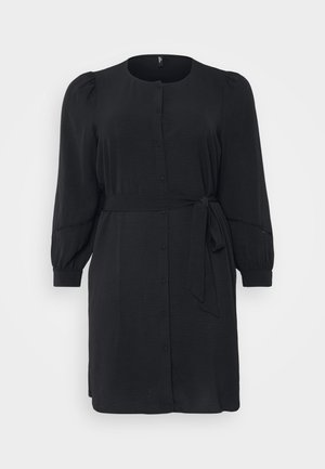 Robe noire en tissu lisse avec un devant à boutons, de longues manches bouffantes et une taille nouée, présentant une silhouette décontractée.