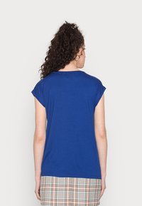 Blue short-sleeve shirt made from soft fabric, featuring a round neckline. Worn over a plaid skirt.