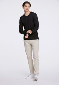 Maglione nero a V con maniche lunghe, design aderente, tessuto texturizzato. Abbinato a pantaloni beige chiaro e sneakers bianche.