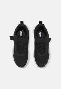 Des chaussures de sport noires présentent un dessus en maille, des lacets et une sangle. La semelle est principalement blanche avec une finition texturée, conçue pour le confort et le soutien.