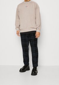 Sudadera beige con logotipo, negra por debajo, combinada con pantalones de cuadros azul marino y zapatos negros gruesos. Ajuste casual con puños acanalados.