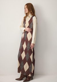 Dolga obleka z vzorcem karo v barvah bordo, krem in siva, s prileganim zgornjim delom in tekočo krilno linijo. Kombinirana z rjavimi koničastimi škornji.