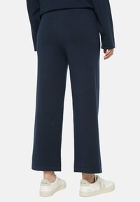 Marinefarbene Weitbein-Hosen aus einem weichen Stoff, mit glatter Oberfläche und gesäumten Kanten. Getragen mit weißen Sneakers.