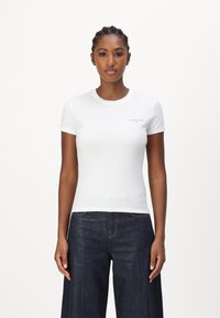 Bílý bavlněný tričko s krátkými rukávy, kulatým výstřihem a malým logem "TOMMY JEANS" na hrudi, zkombinované s tmavými džínovými kalhotami širokého střihu.