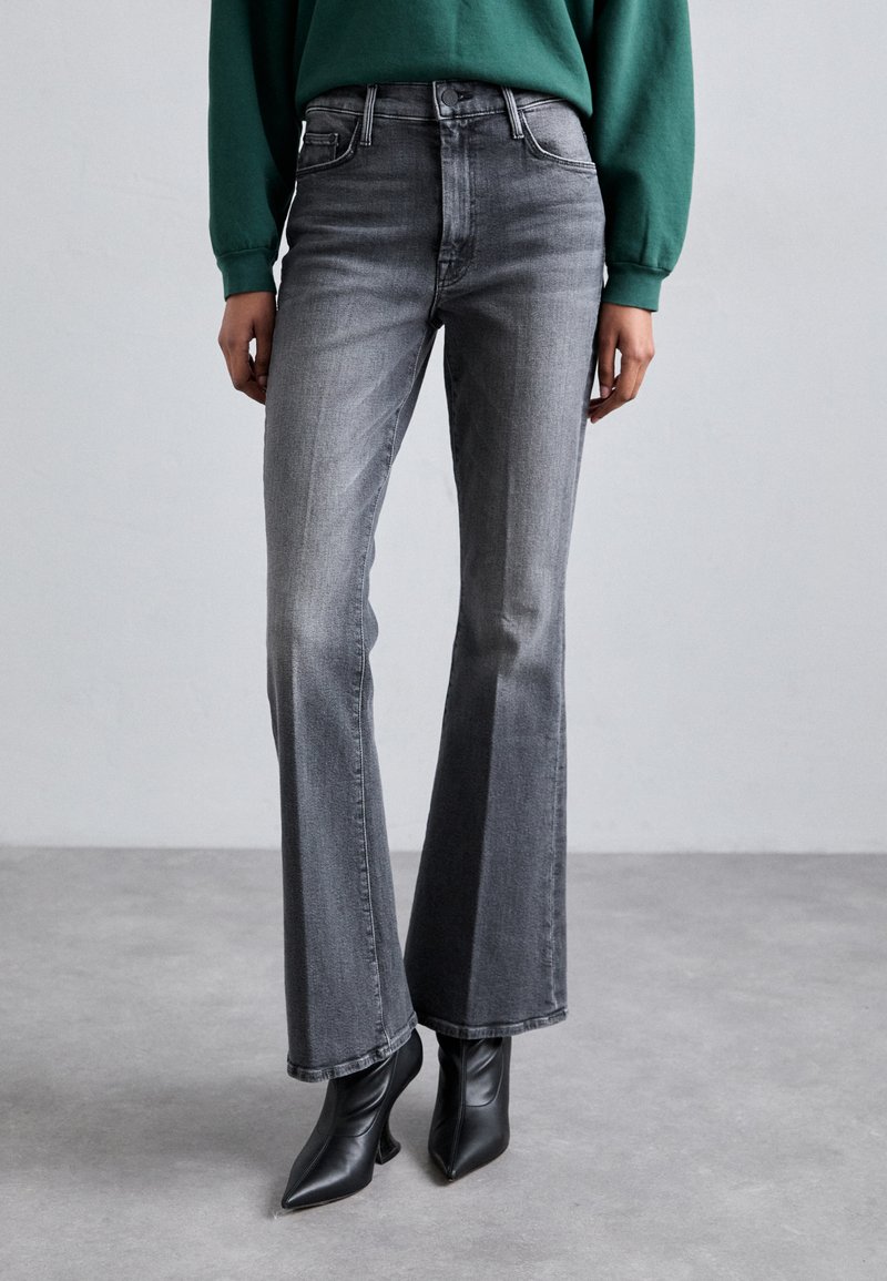 Jeans in denim grigio a zampa d'elefante con vita alta, caratterizzati da un leggero sbiadimento, cinque tasche e cuciture a contrasto, abbinati a tacchi neri a punta.
