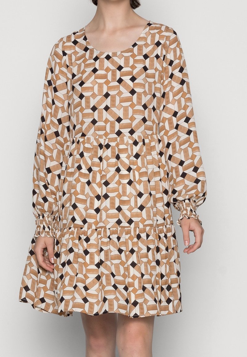 Robe beige à manches longues avec motif géométrique de cubes en blanc, marron et noir, dotée d'une taille froncée et d'un ourlet à volants.