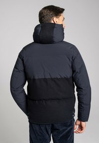 Padded jacket w kolorze czarnym i granatowym w blokach kolorystycznych. Posiada wysoki kołnierz oraz przyciski na dolnej krawędzi, wykonana z gładkich i teksturowanych materiałów.
