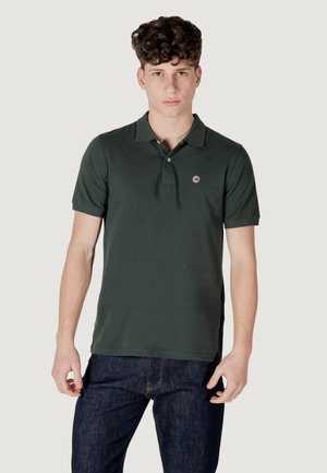 Polo shirt verde a maniche corte realizzato in cotone, caratterizzato da un colletto classico e un piccolo logo ricamato sul lato sinistro del petto. I jeans sono di colore blu scuro.