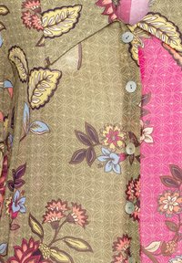 Chemise à motif floral avec des sections vert olive et rose, tissu léger, détails de boutons et dessins distincts de feuilles et de fleurs.