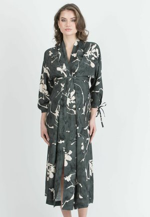 Abito a rappezzo nero a fiori con accenti crema, caratterizzato da maniche lunghe, vita con cinture e spaccature laterali per facilitare il movimento. Tessuto liscio e leggero.