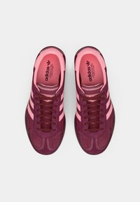 Ματζέντα και ροζ αθλητικά παπούτσια με υφασμένο άνω μέρος από σουέντ, τρεις ροζ ρίγες και καφέ λαστιχένια σόλα. Κορδόνια σε σκούρο ματζέντα.