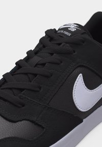 Κοντινή λήψη μαύρου παπουτσιού Nike SB Delta Force με μαύρα κορδόνια, λευκό λογότυπο Nike και υφή σόλας πάνω σε λευκό φόντο.