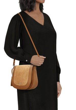 Tan leren crossbody tas met een suède klep, met een gladde textuur, verstelbare strap en franje detail. Close-up van een persoon die het vasthoudt.